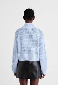 Ανοιχτό μπλε πλεχτό πουλόβερ με rib κολλάρο και στρίφωμα, χαρακτηρισμένο από μια υφασμένη υφή και cropped σχέδιο. Φορεμένο πάνω από μια μαύρη δερμάτινη μίνι φούστα.