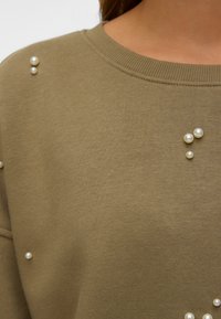 Olijfgroen trui met een textuurafwerking, voorzien van decoratieve parelaccenten op de schouder in verschillende maten. Klassiek rondhalsontwerp.