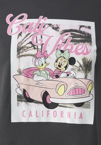 Camiseta gráfica con un coche vintage rosa, personajes de dibujos animados Minnie y Daisy, un fondo de palmeras en blanco y negro, y el texto "Cali Vibes".