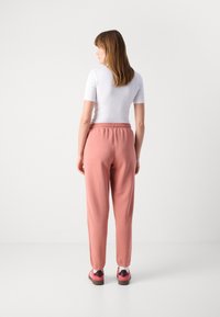 Roze sweatpants met elastische tailleband, taps toelopende pijpen en boordjes bij de enkels. Gecombineerd met een witte aansluitende top en roze schoeisel.