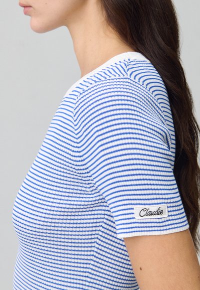 Top lavorato a maglia a righe blu e bianche con una forma aderente. Presenta un collo rotondo e una piccola etichetta sulla manica con la scritta "Claudie."