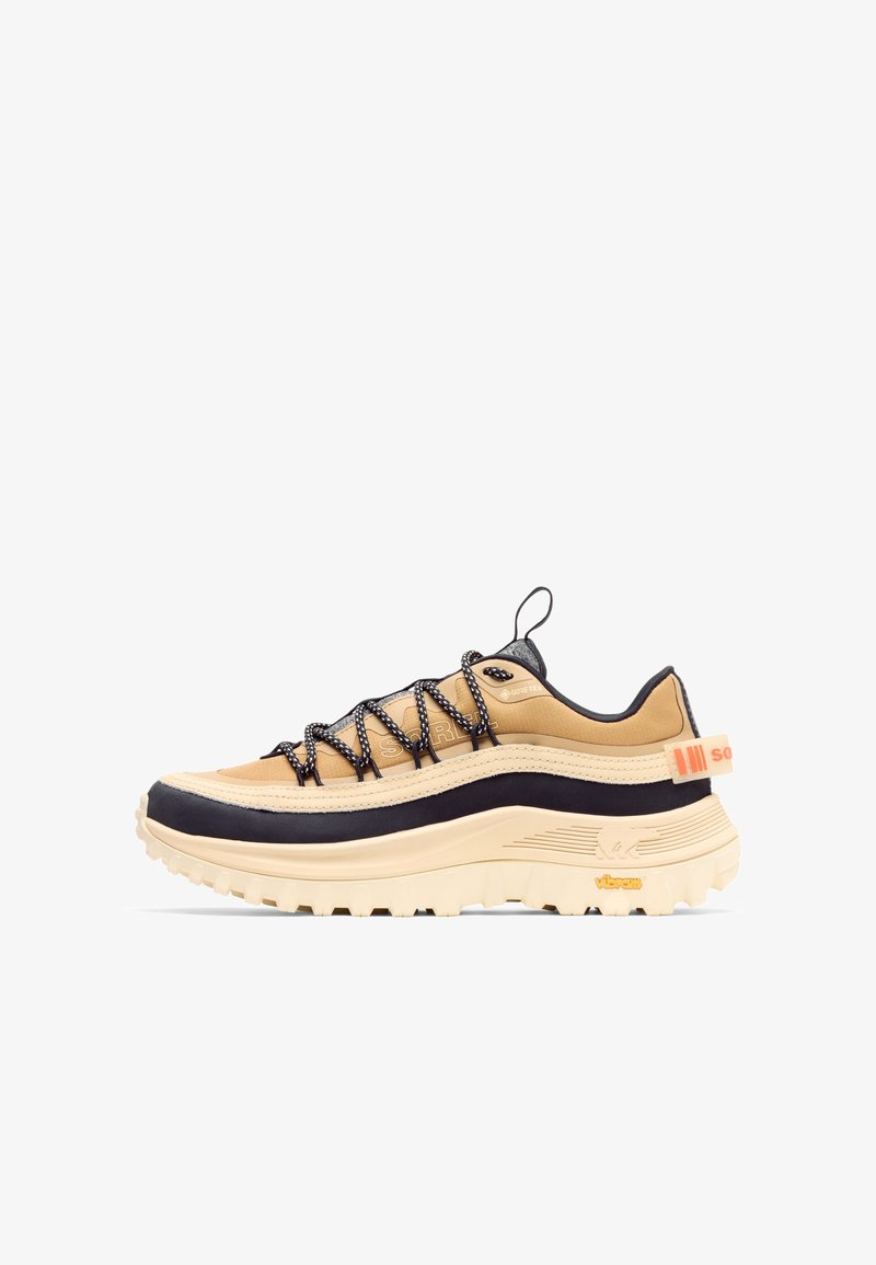 Baskets de randonnée basses de couleur marron clair et noire avec une semelle épaisse beige, des lacets noirs et blancs, une étiquette Gore-Tex et une languette arrière avec un détail orange.
