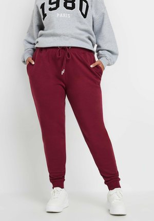 Bordeaux-coloured sweatsitkämmät, joissa on elastisk vyötärö ja külje taskud, koos halli kapuutsiga särgiga, millel on must graafiline print. Valged tennisetossud.