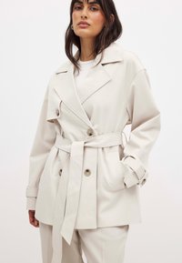 Šviesiai rudas paltas su diržu ties liemeniu, dvigubais sagomis ir didelėmis apykaklėmis. Pagamintas iš švelnaus audinio, laisvo kirpimo ir su šoninėmis kišenėmis.