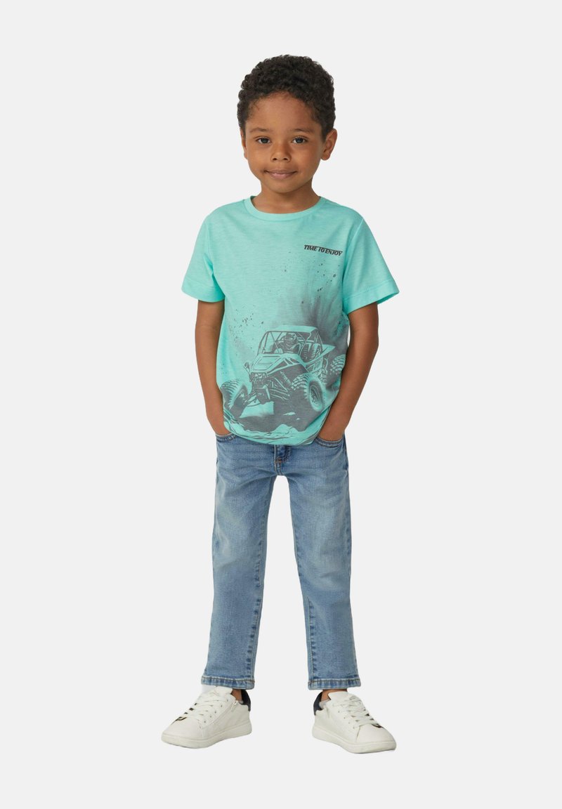 Muntgroene katoenen t-shirt met een afbeelding van een off-road voertuig, gecombineerd met lichtblauwe denim jeans en witte sneakers.