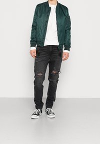 Zelená bombardérka, bílá dlouhá košile, černé roztrhané džíny s dírami a černo-bílé tenisky. Hladký materiál, ležérní design.