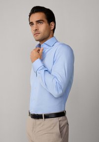 Camicia azzurro chiaro con un motivo a quadri, colletto button-down, maniche lunghe e bottoni, abbinata a pantaloni beige chiaro e una cintura nera.