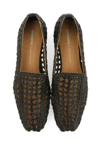 Zapatos negros de tejido trenzado tipo slip-on con perforaciones abiertas, punta cuadrada y una plantilla marrón que presenta el nombre de la marca. Diseño ligero para mayor transpirabilidad.