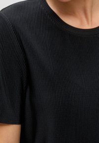 Camiseta negra de canalé con cuello redondo y mangas cortas. La textura de la tela es suave con canalés verticales en toda su extensión.