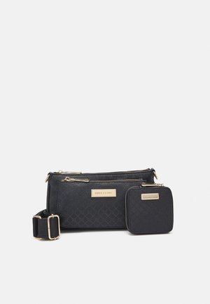 Musta teksturoitu olkalaukku ja siihen sopiva neliskulmainen kolikkopussi, joissa molemmissa on kullanväriset vetoketjut ja säädettävä hihna vaalealla taustalla.