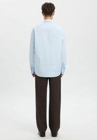 Lyseblå og hvitstripet skjorte med avrundet kant, knappede mansjetter og en klassisk krage, kombinert med mørkebrune bukser med vide ben.