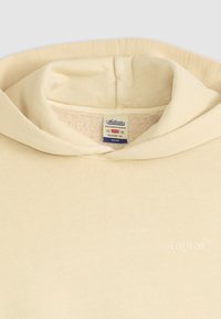 Crème-kleurige hoodie met een zachte, gestructureerde binnenkant. Heeft een ronde hals en een klein, verdiept logo aan de voorkant. Relaxte pasvorm.