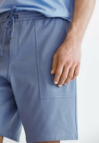 Shorts bleus en tissu doux, avec une poche latérale ornée de coutures et une taille ajustable avec cordon de serrage.