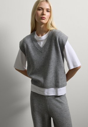 Grijze gebreide vest met een V-hals, mouwloos ontwerp, gedragen over een wit T-shirt. Zachte textuur en geribbelde zoomdetails, gecombineerd met bijpassende broek.