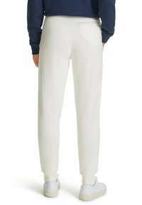 Weiße Sweatpants mit gerippten Bündchen und einer Gesäßtasche, aus einem weichen Stoff gefertigt, kombiniert mit weißen Turnschuhen.