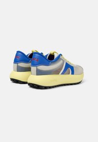 Sneaker con una tomaia in mesh grigia e blu, suola in gomma gialla e marchio rosso. Presenta una forma arrotondata e dettagli testurizzati.