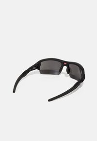 Czarne okulary przeciwsłoneczne o matowym wykończeniu, z oprawką typu wrap-around, ciemnymi soczewkami i ergonomicznymi zausznikami. Posiadają detal z logo w pobliżu zawiasów.