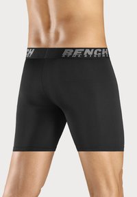 Black boxer briefs with a wide elastic waistband featuring "BENCH" branding. Smooth, stretchy fabric and mid-thigh length.