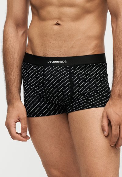 Torse masculin portant un boxer noir avec un texte blanc diagonal "DSQUARED2" et une ceinture noire unie avec un logo blanc "DSQUARED2" centré.
