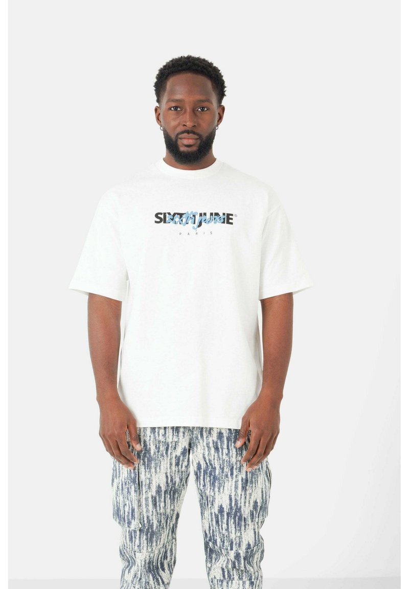 Witte t-shirt met korte mouwen met een blauwe grafische tekst "SIGNATURE PARIS" op de voorkant, gecombineerd met gestructureerde blauw-witte gestreepte broek.