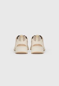 Beige joggesko med teksturert overdel, polstret hæl og gummisåle. Har to trekkflapper og et perforert design for pusteevne.