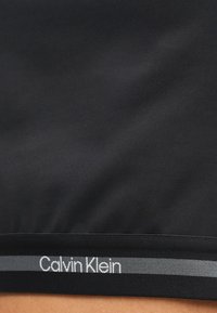 Μαύρο ύφασμα με λεία υφή, με οριζόντιο λωρίδα στη μέση που φέρει το λογότυπο «Calvin Klein» σε λευκό και μια γκρι διακριτική ρίγα.