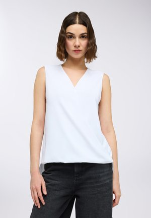 Top bianco senza maniche con scollatura a V, tessuto liscio, vestibilità comoda e orlo asimmetrico; abbinato a jeans scuri.