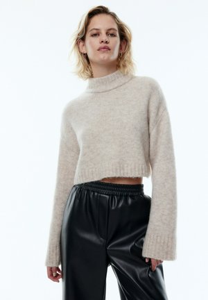 Hellbeige, kurz geschnittenes Turtleneck-Pullover aus weichem Material mit Rippenabschluss, kombiniert mit hochgeschnittenen schwarzen Kunstlederhosen.
