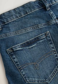 Jeans de denim con un lavado azul clásico, un bolsillo trasero y costuras en amarillo contrastante. Tejido texturizado con un aspecto usado.