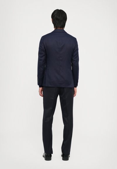 Navy suit jacket with a tailored fit, single vent at the back, and matching trousers. Black shoes complete the outfit.
