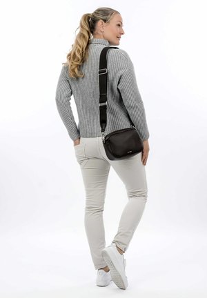 Borsa crossbody in pelle marrone con finitura testurizzata e tracolla regolabile. Modello che indossa un pullover grigio a coste e pantaloni beige chiaro, di spalle.