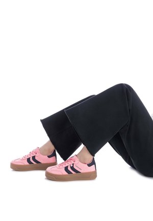 Zapatillas de ante rosa con acentos negros, punta redonda y suela de goma gruesa. Combinadas con pantalones de pierna ancha negros con dobladillos deshilachados.