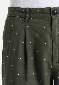 Olive zelené kalhoty s bílými puntíky, s knoflíkovým uzávěrem, nařaseným předním dílem a jemnou bavlněnou texturou.