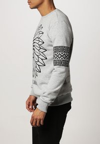 Gray sweatshirt with a large black graphic of flower petals on the front and a patterned black band on the right sleeve. Ribbed cuffs and hem.
