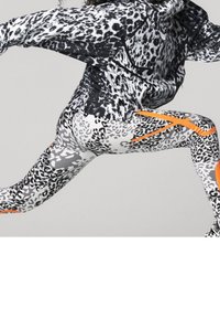 Svart och vit leopardmönstrad jacka med grå och vit leopardmönstrade leggings som har orange accenter, designad för aktiv rörelse.