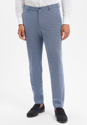 Schmale Herrenhose in Hellblau, kombiniert mit schwarzen Loafers und einem weißen Hemd, dargestellt von der Taille bis zu den Füßen vor einem schlichten weißen Hintergrund.