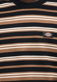 Svart, brun og hvit stoff med horisontale striper og en liten rektangulær Dickies-logo på brystområdet.