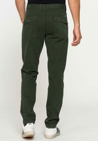 Pantaloni cargo verdi in cotone con vestibilità dritta, due ampie tasche posteriori e un discreto patch del marchio, abbinati a sneakers sportive bianche.