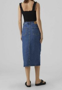 Svart smockad linne med volangärmar, matchat med en högmidjad, lång blå denimkjol med två bakfickor och en rak siluett.