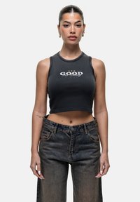 Top corto nero con scollatura rotonda, con la scritta bianca "GOOD" e tre stelle. Indossato con jeans a vita alta blu scuro.