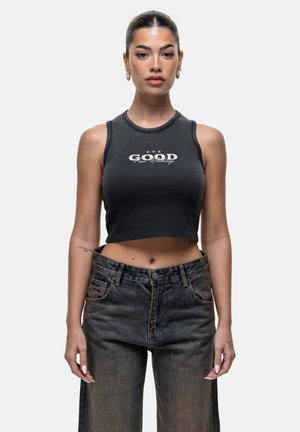 Black cropped tank top with a round neckline, featuring white text "GOOD" and three stars. Worn with dark blue high-waisted jeans.