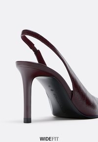 Slingback stiletto bordeaux con finitura testurizzata, punta affusolata e tacco alto. Presenta una cinghia alla caviglia regolabile e una base solida.