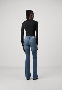 Bodycon nero a maniche lunghe, abbinato a jeans svasati blu con un classico stile a cinque tasche e una finitura chiara.