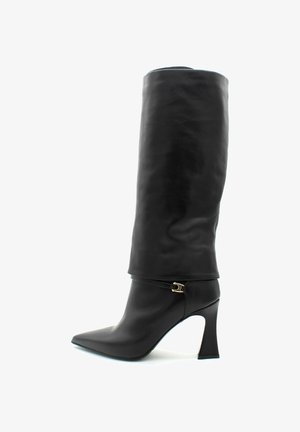 Botte noire en cuir jusqu'au genou avec un bout pointu, une sangle fine et une boucle en or, et un talon haut évasé sur fond blanc.