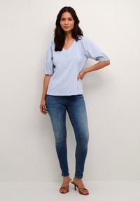 Kék és fehér csíkos blúz V-nyakkal és puffos ujjal, illeszkedő kék farmernadrággal és barna, pántos magassarkú cipővel párosítva. Sima textúra, hétköznapi dizájn.