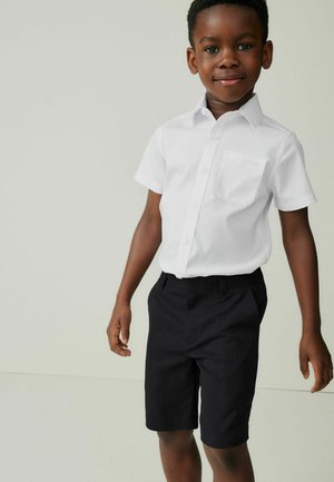 Hvid kortærmet skjorte med en brystlomme og mørkegrå shorts. Skjorten er knappet, og outfittet har et rent, minimalistisk design.