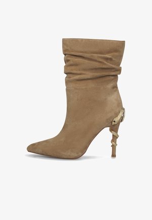 Beige Wildleder-Ankle-Boot mit einem lässigen Design, spitzem Schuhkopf und einem goldenen Schlangenakzent an der Ferse. Glatte Textur und schlanke Form.