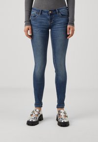Tanke modre denim hlače z srednjim pasom, petimi �žepi in subtilnimi madeži. Ujemajo se s sijočimi srebrnimi platform čevlji.