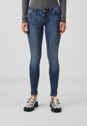 Skinny blue denim jeans with a mid-rise waist, five pockets, and subtle fading. Paired with shiny silver platform shoes.
