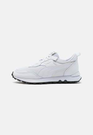 Baskets blanches de sport avec fermeture à lacets, dessus en mesh et cuir, semelle noire texturée sur fond clair uni.
